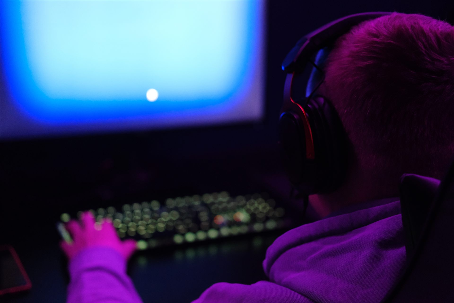 Young gamer wearing a headset, lit by screen glow in a dark room